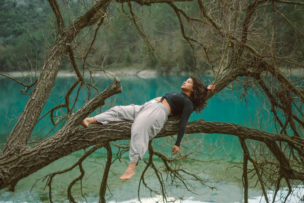 A woman laying on a tree branch near a lake